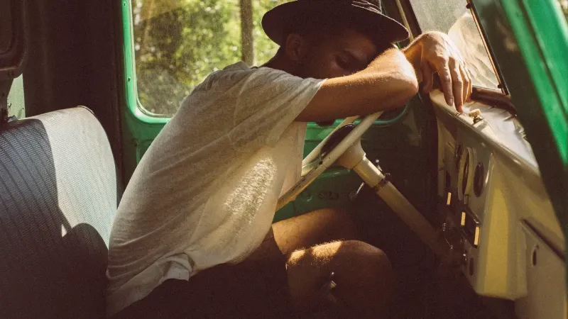 a man sleeping in a vehicle with his head on the steering wheel