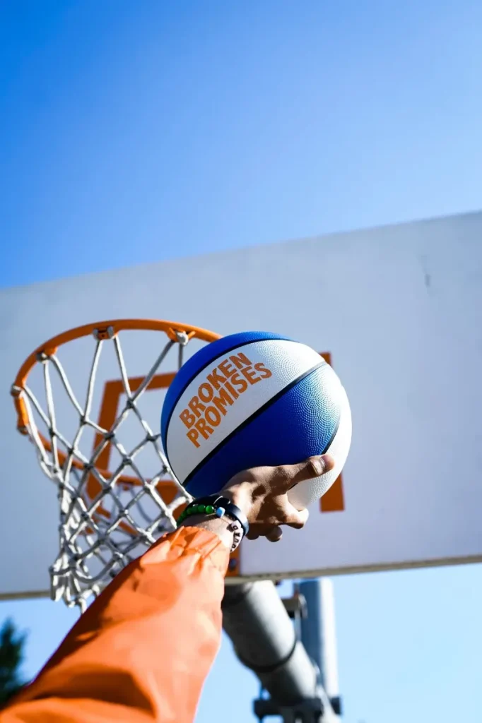 a human laying a basketball with Broken Promises labeled on it towards a hoop