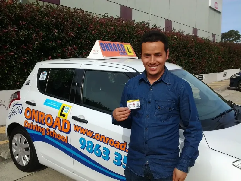 man holding his license in front of a driving school car