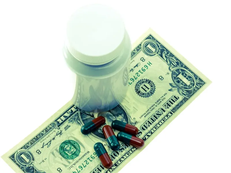 medication bottle and pills on top of a $1 bill