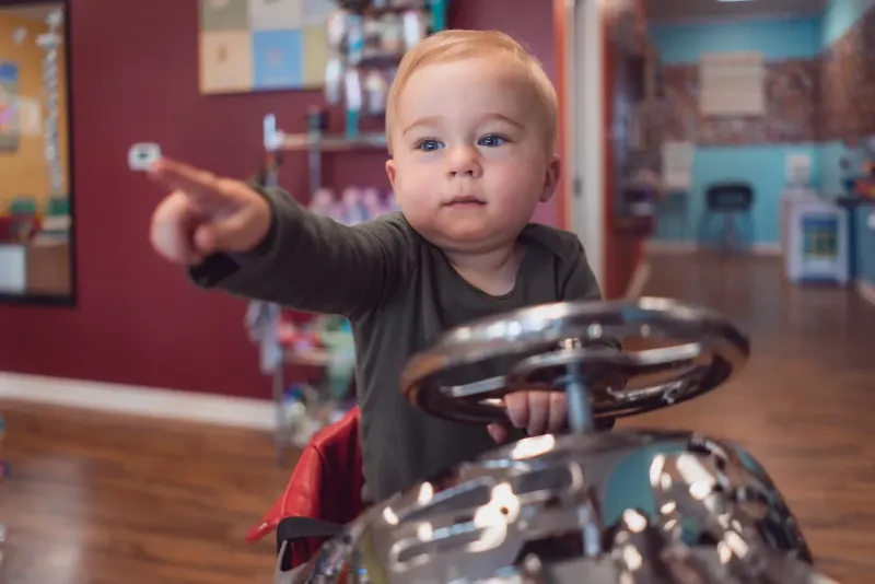 child pointing while sitting on a toy car