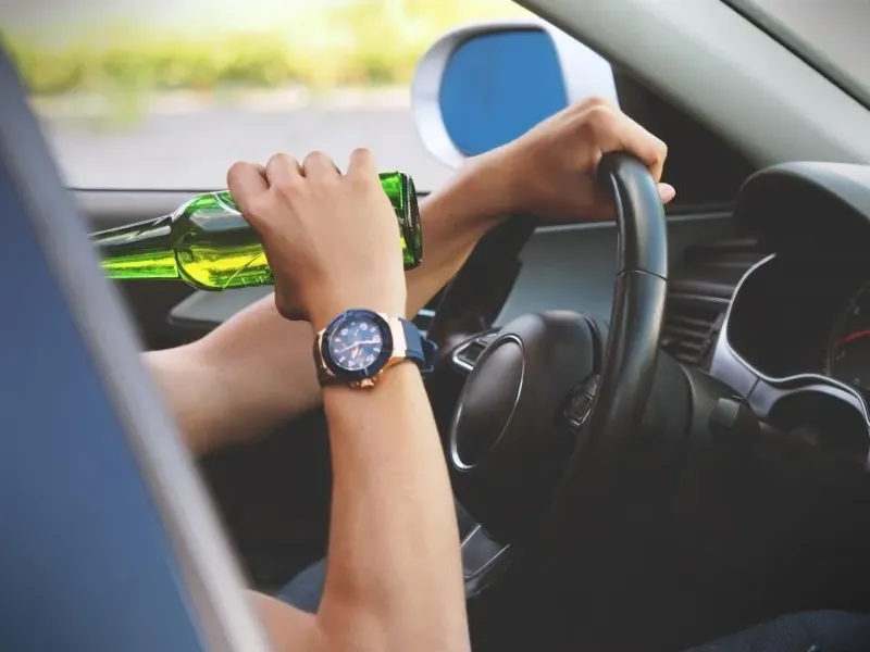 a person drinking a bottled beer behind the steering the wheel