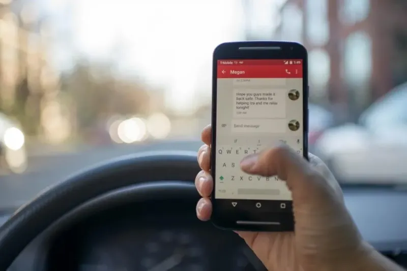 person looking at a text message on their phone behind the steering wheel