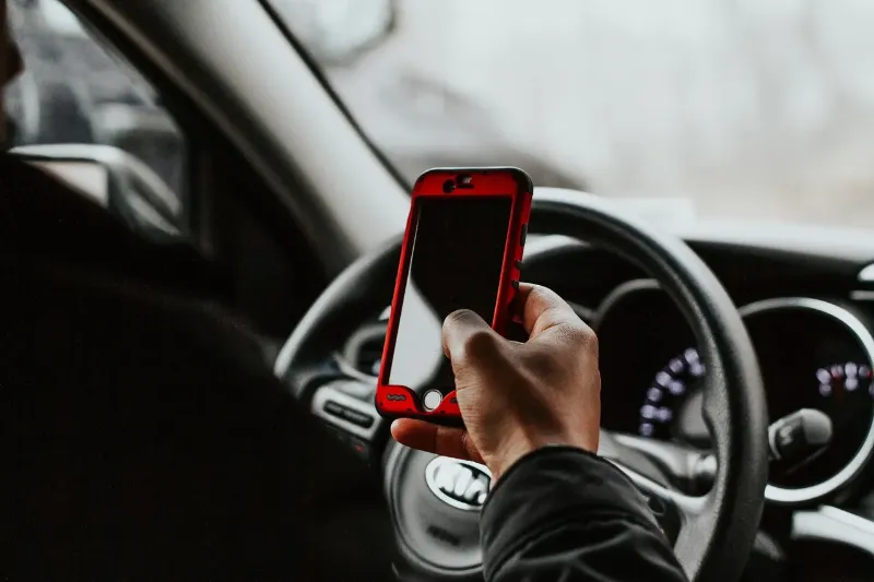 person on their mobile behind their KIA steering wheel